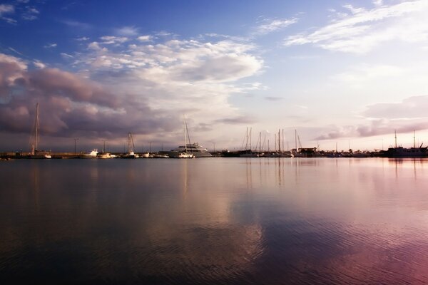 Күн батқан кезде жағалаудағы яхталардың силуэттері